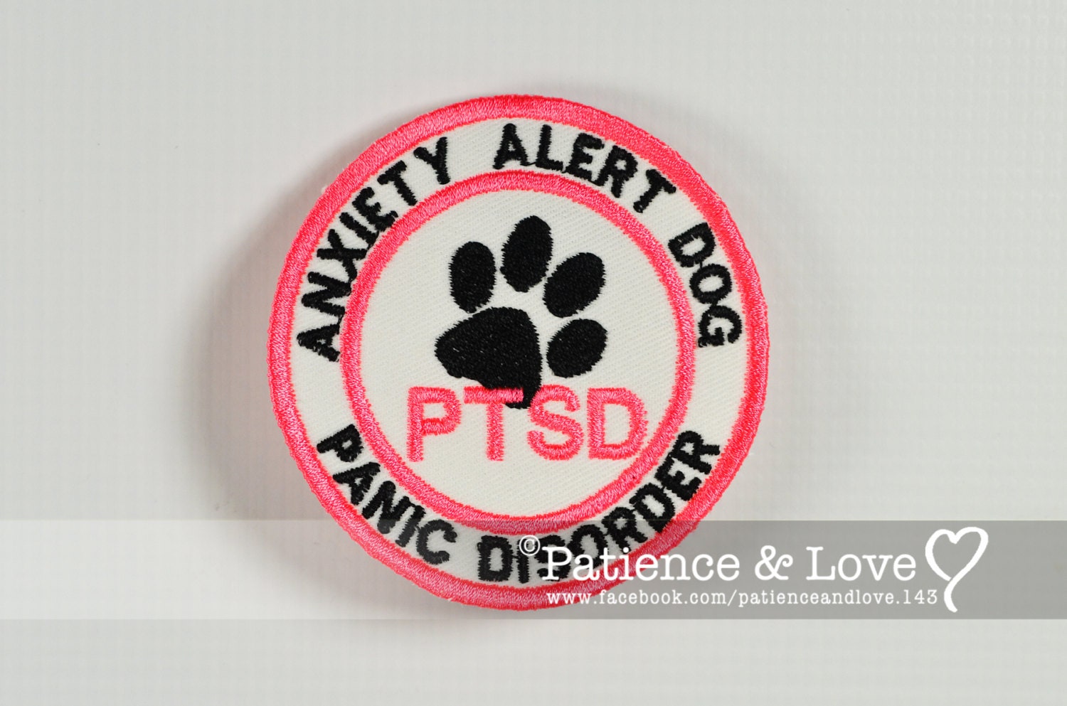 "ANXIETY ALERT DOG - PANIC DISORDER" around the top and bottom.  In the center it says PTSD with a paw print   As seen in the listing photo. The listing photo shows white fabric, pink (1909) for the PTSD and edge, black text.